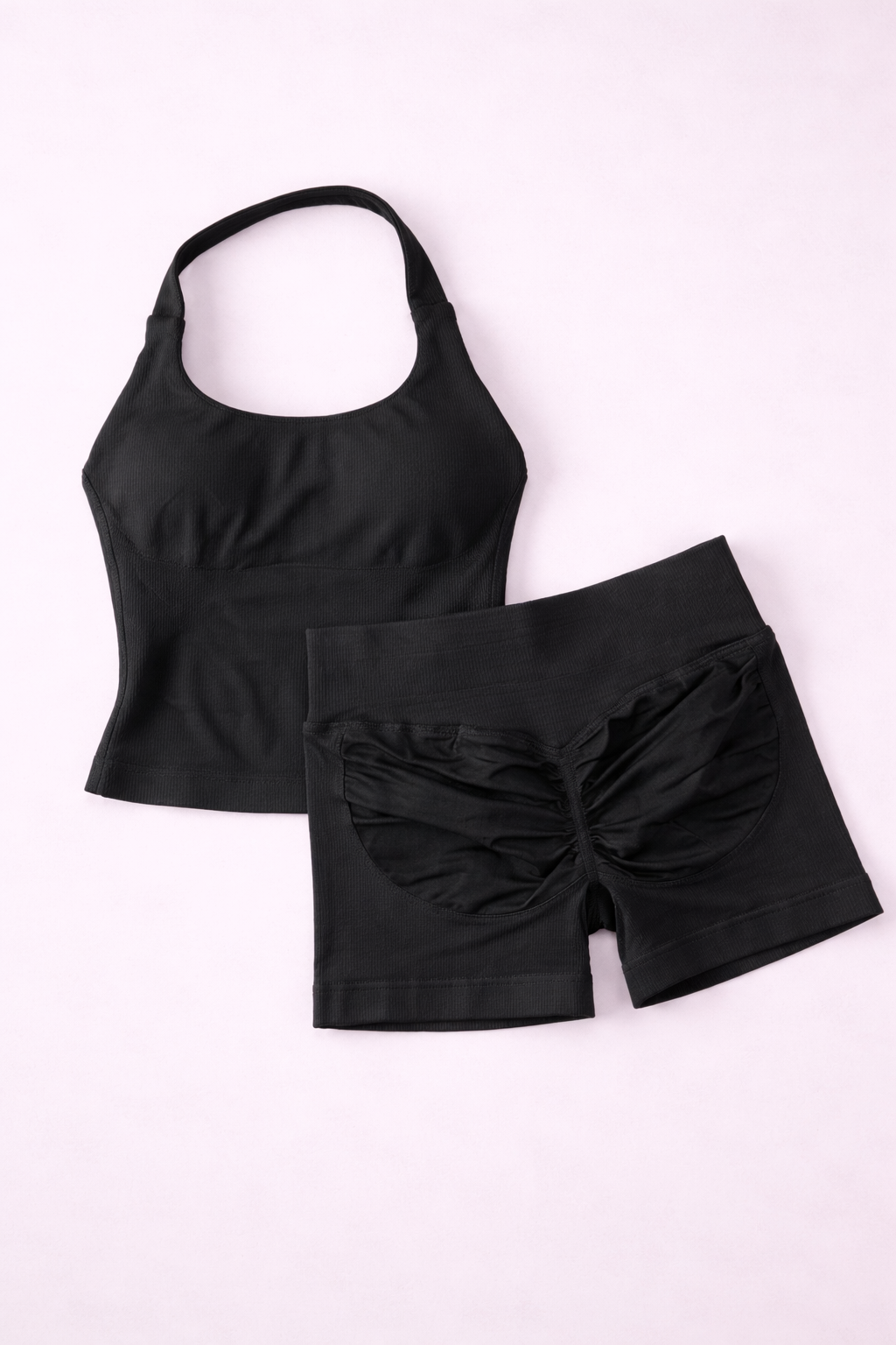 Ensemble activewear femme ALYA Black GLIIMA présenté à plat, composé d’un haut ajusté col halter et d’un short taille haute avec léger scrunch au dos.