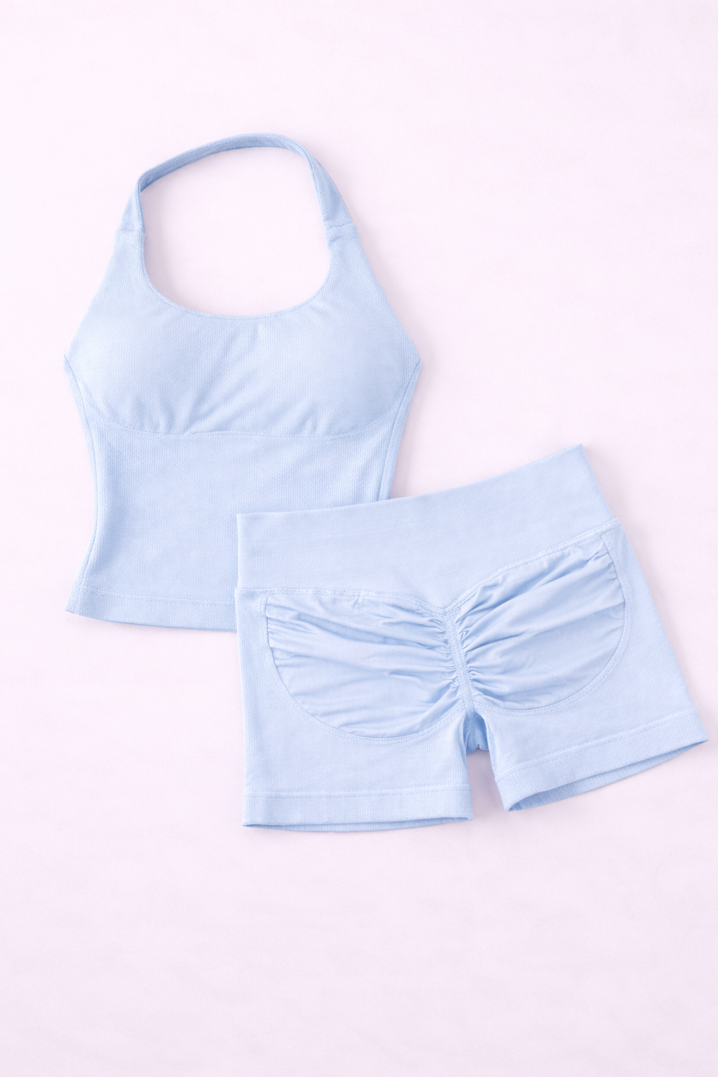 Ensemble activewear femme ALYA Ice Blue GLIIMA présenté à plat, composé d’un haut ajusté col halter et d’un short taille haute avec léger scrunch au dos.